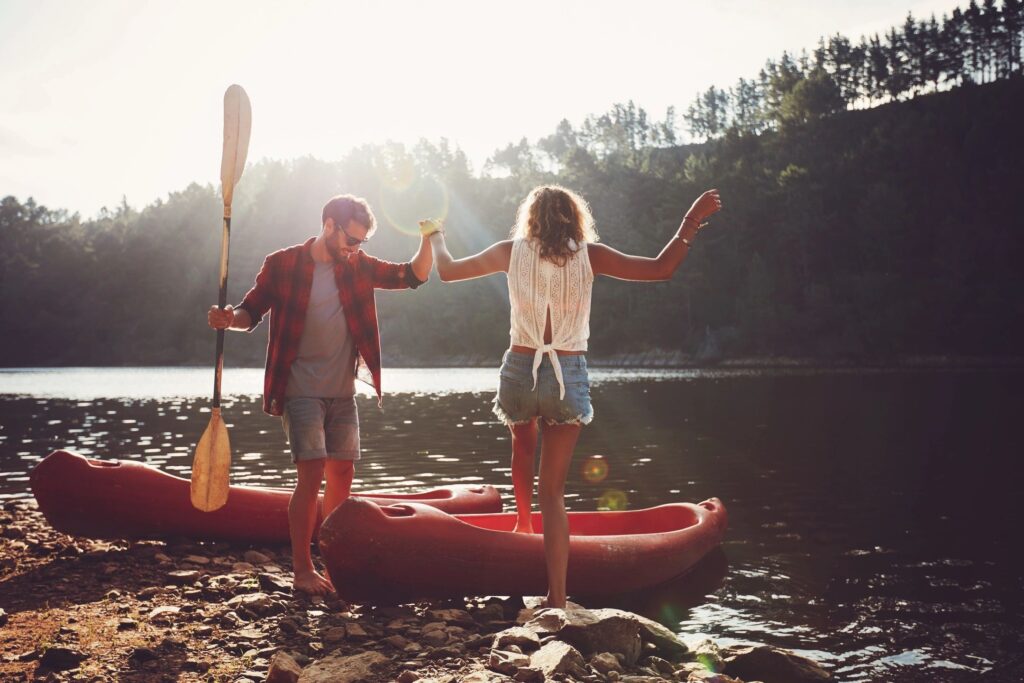 Couple balancing on a kayak by a lakeside at sunset.