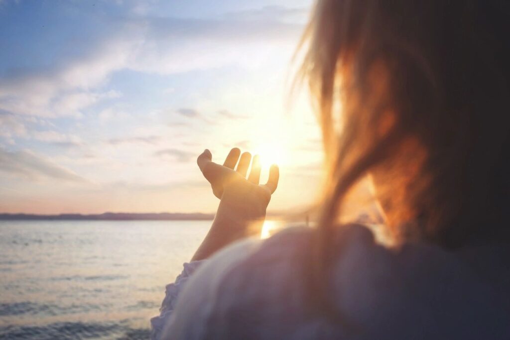 Person reaching out toward the sunset over water.