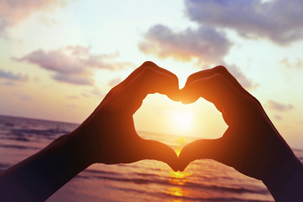 Hands forming a heart shape with a sunset in the background.
